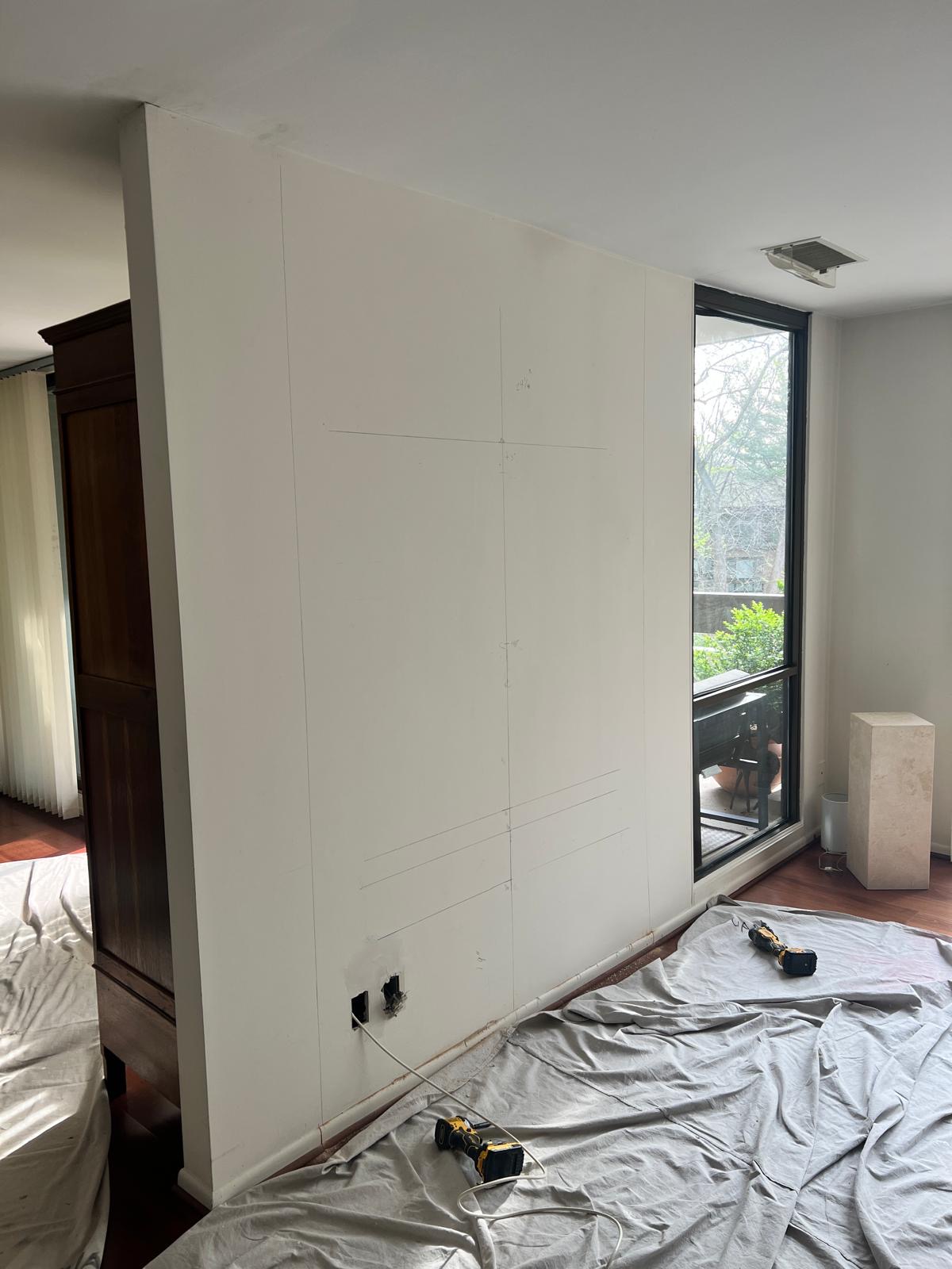 Before — plain wall marked and cut for a recessed TV niche, with drop cloths and tools
