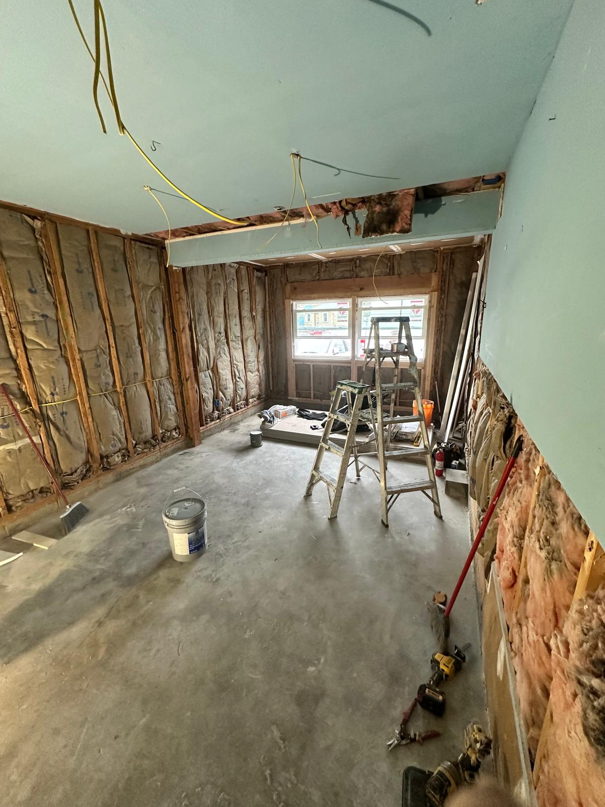 Before — room gutted to the studs with exposed insulation, wiring and ladders during renovation