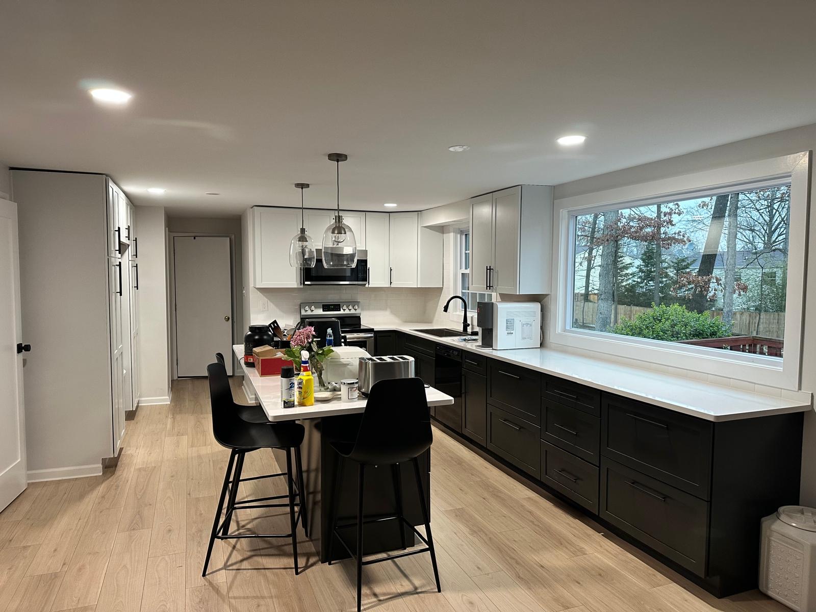 After — finished kitchen with black island cabinets, white counters and pendant lights