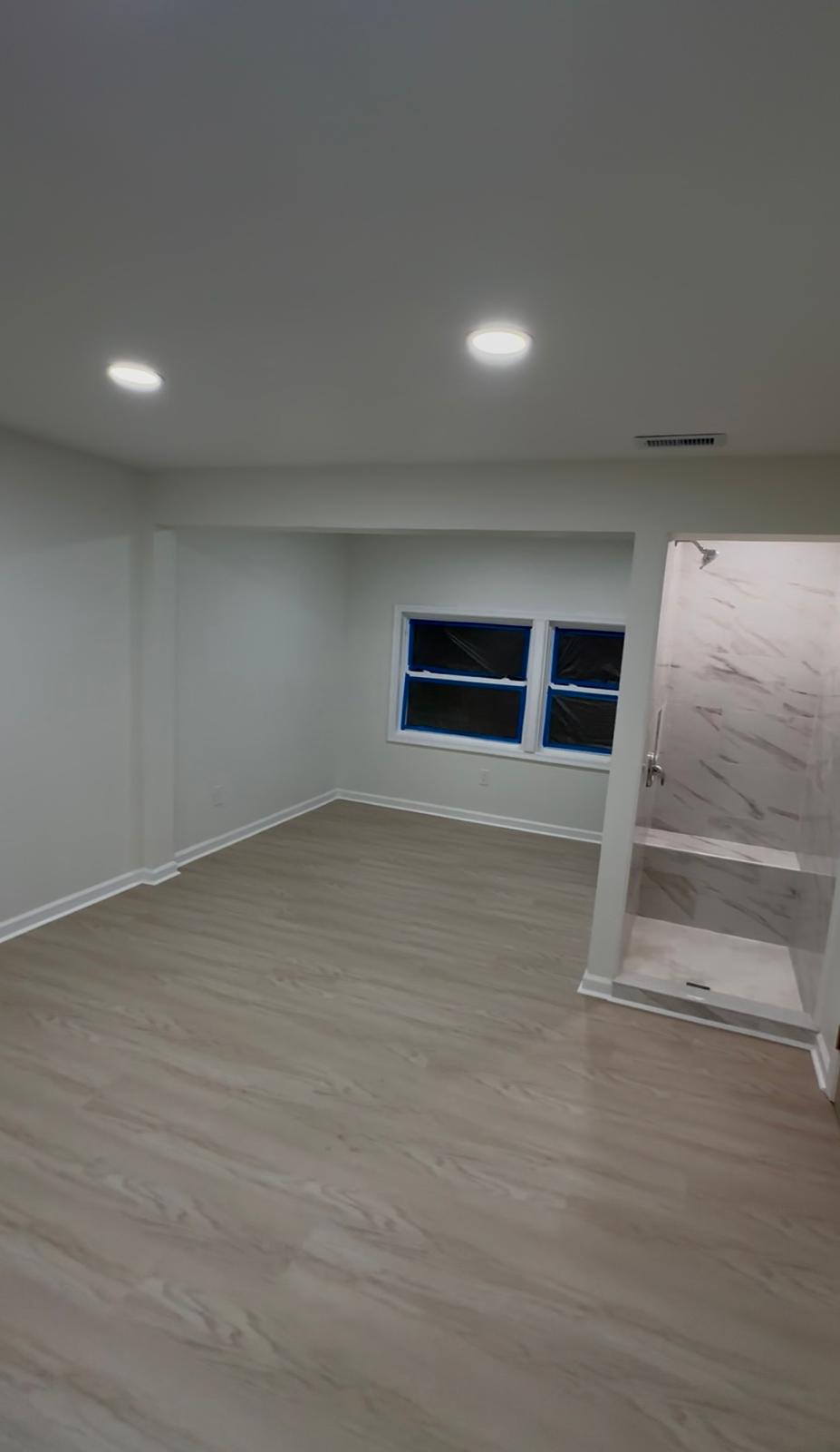 After — finished room with freshly painted walls, new flooring, recessed lights and a tiled shower